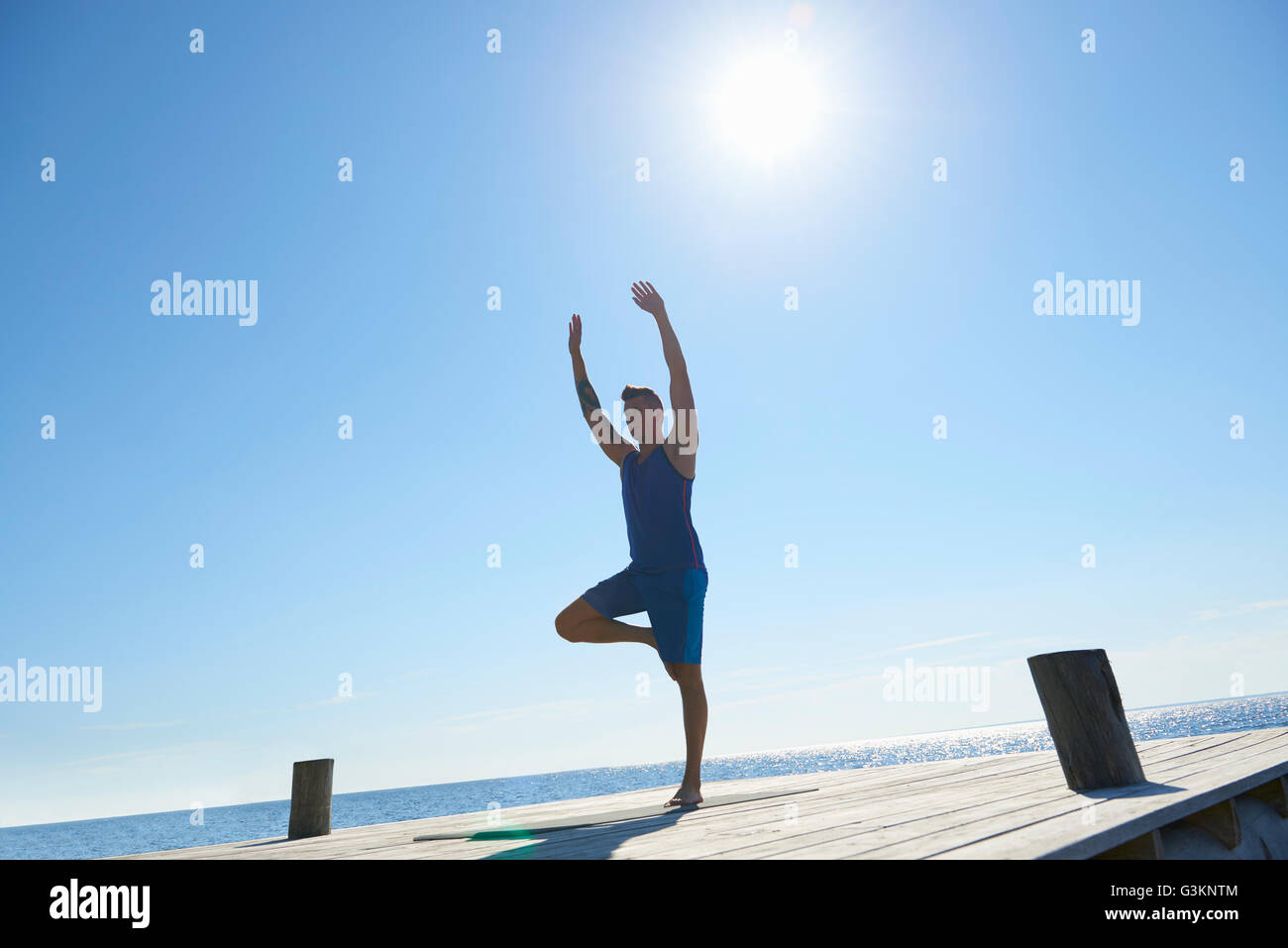 Mann am Pier stehen auf einem Bein erhobenen Armen Ausübung Stockfoto
