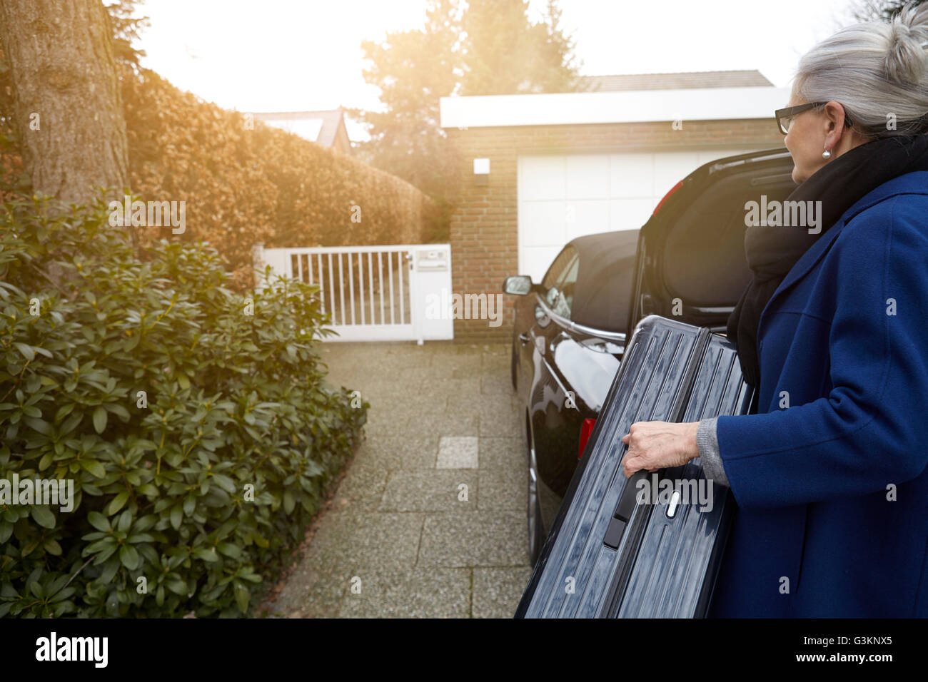 Frau auf der Zufahrt vor offenen Kofferraum mit Koffer Stockfoto