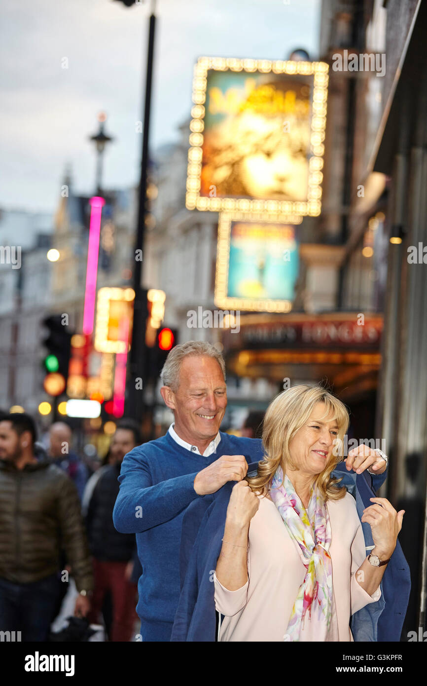 Reifer Mann anziehen Jacke über Freundinnen Schultern Stadt Straße in der Abenddämmerung, London, UK Stockfoto