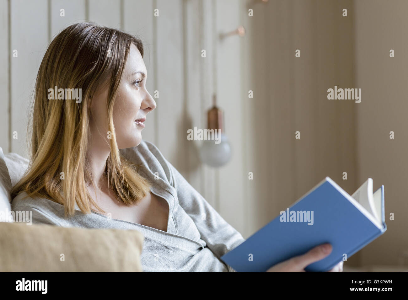 Frau sitzt auf dem Bett, hält Buch wegschauen Stockfoto