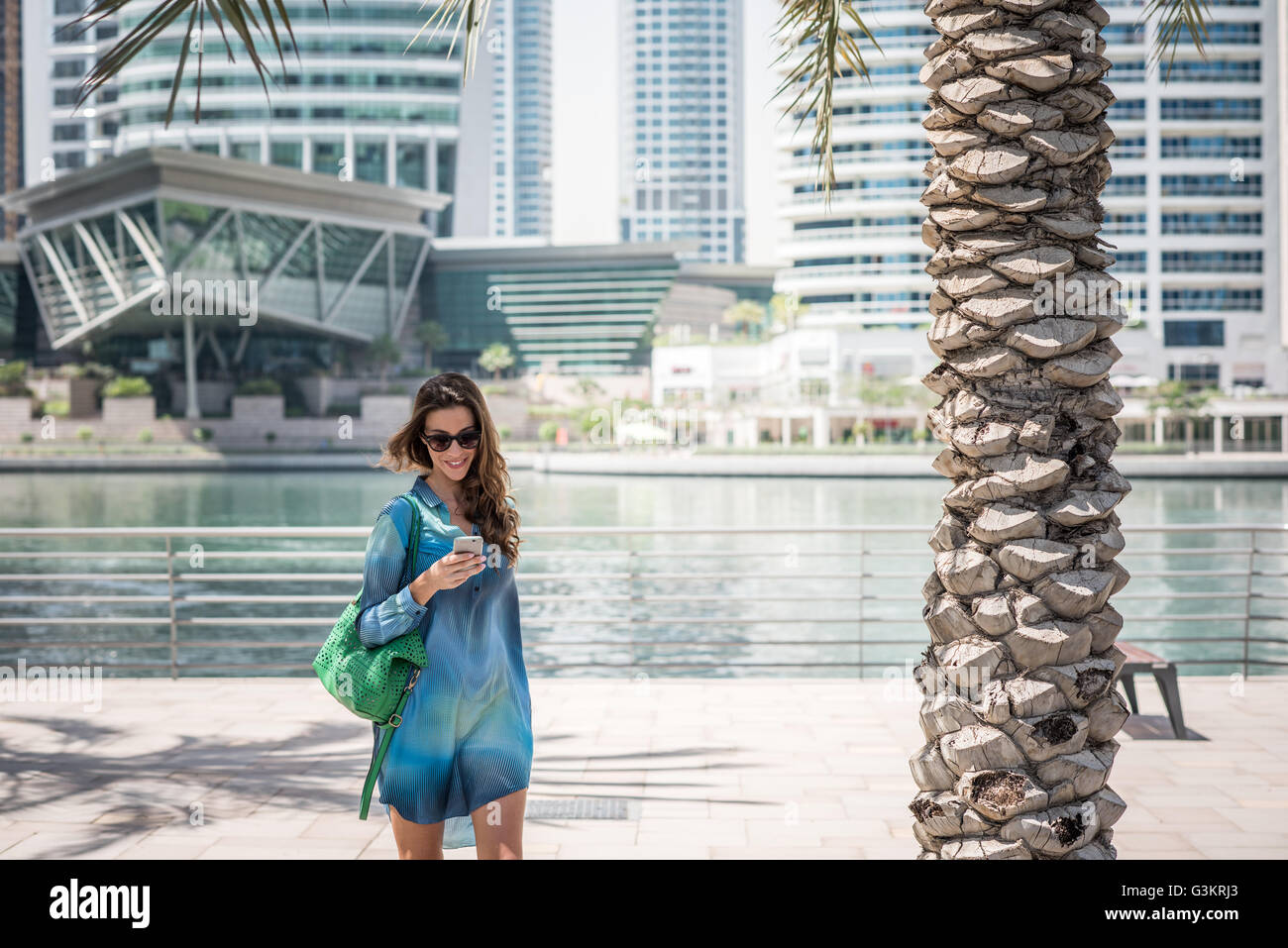 Weibliche Touristen Flanieren am Wasser lesen Smartphone Texte, Dubai, Vereinigte Arabische Emirate Stockfoto