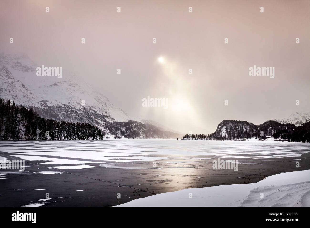 Sonnenstrahlen auf zugefrorenen See und Schnee bedeckt Berge, Engadin, Schweiz Stockfoto