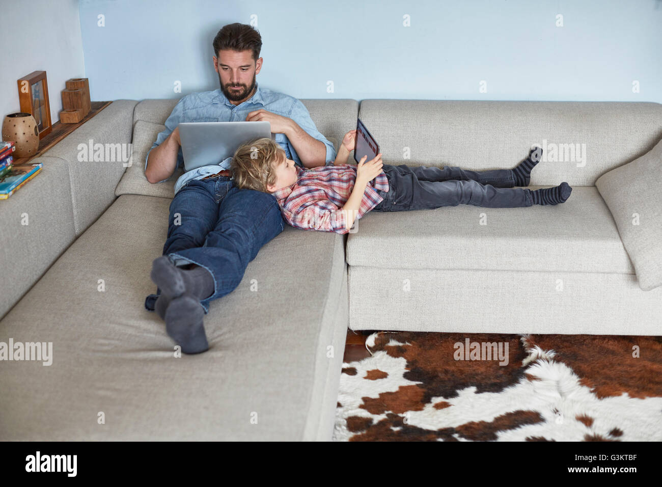 Junge auf Sofa liegend mit Vater-Technologie Stockfoto Junge auf Sofa liegend mit Vater-Technologie Stockfoto