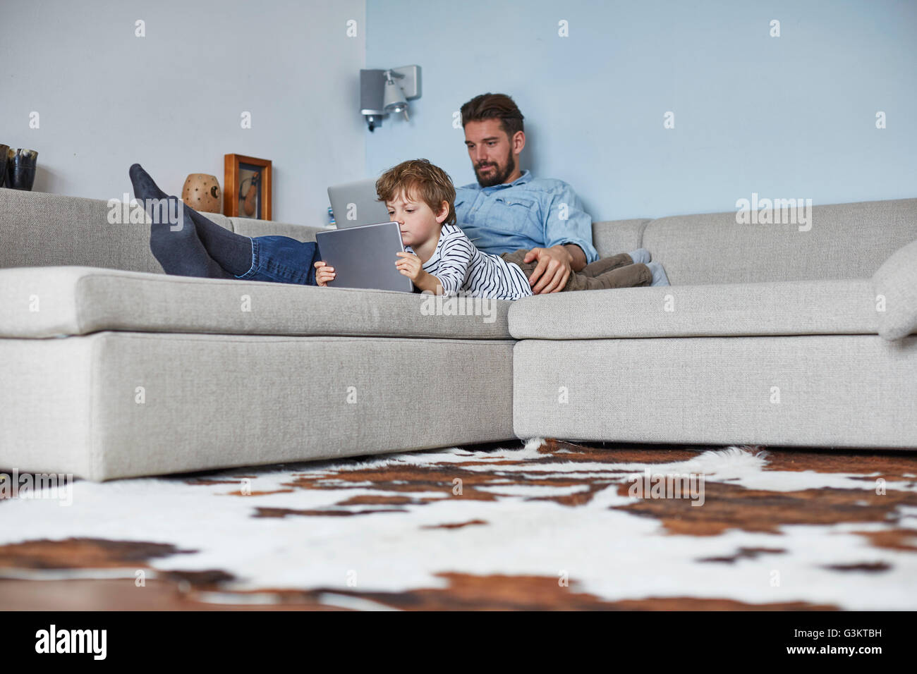 Junge auf Sofa liegend mit Vater-Technologie Stockfoto Junge auf Sofa liegend mit Vater-Technologie Stockfoto