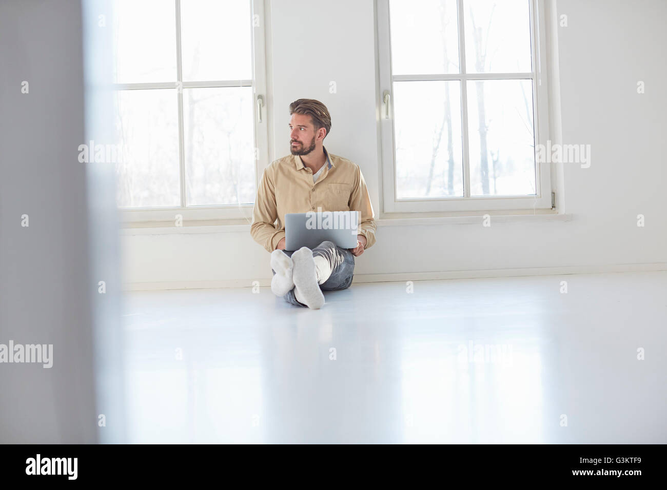 Junger Mann am Boden mit Laptop in leeren neuen Zuhause Stockfoto