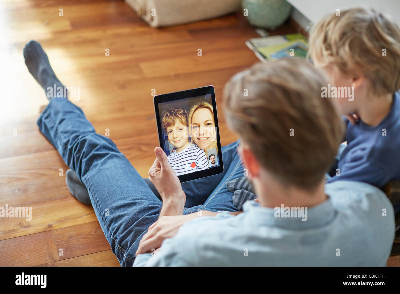Mann und Sohn sitzen auf Boden Gespräch mit Mutter und Bruder auf digital-Tablette Videoanruf Stockfoto