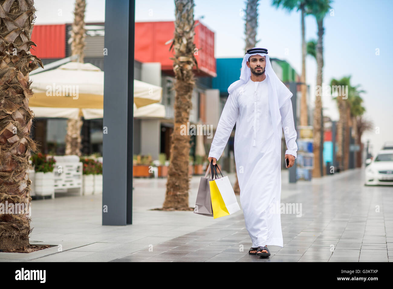 Mann trägt traditionelle orientalische Kleidung zu Fuß entlang der Straße Shopping Tragetaschen, Dubai, Vereinigte Arabische Emirate Stockfoto