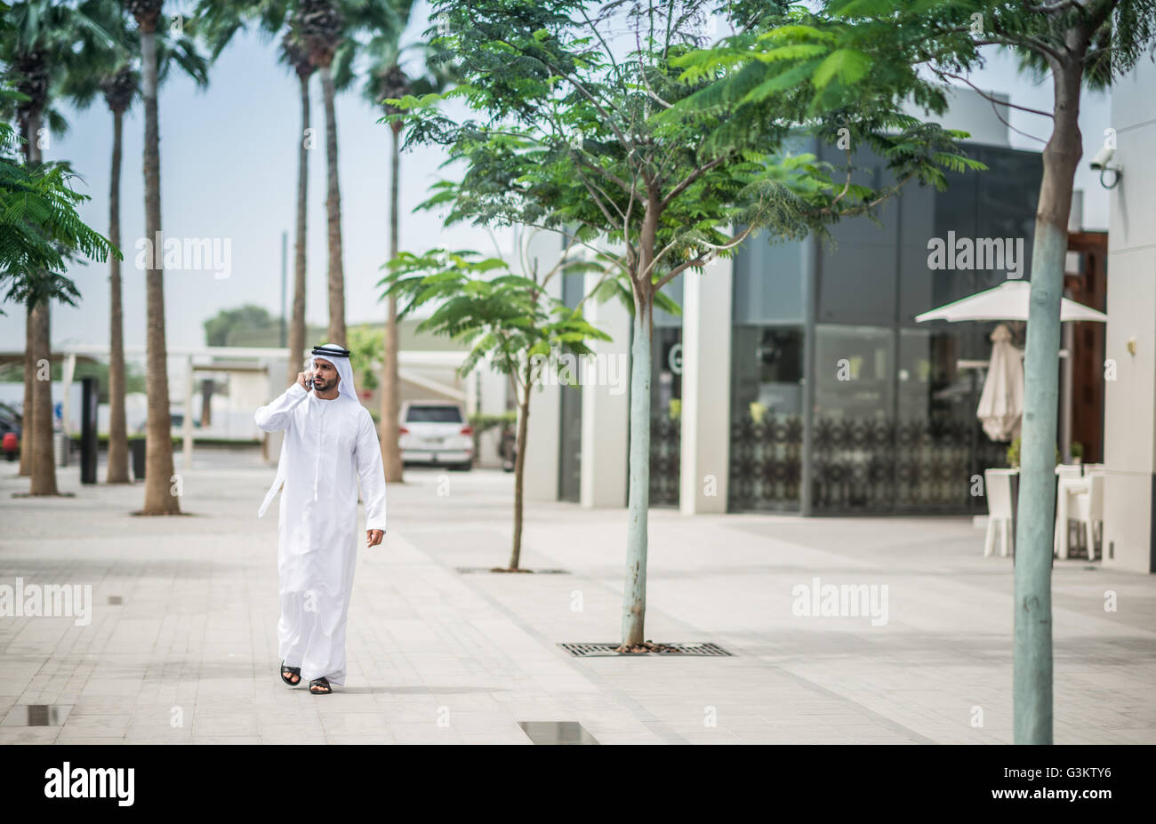 Mann trägt traditionelle orientalische Kleidung zu Fuß entlang der Straße sprechen auf Smartphone, Dubai, Vereinigte Arabische Emirate Stockfoto