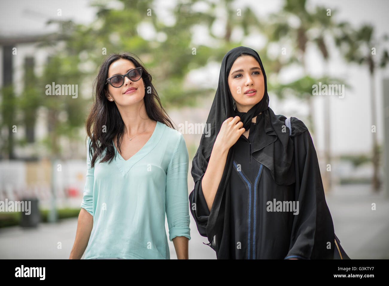 Junge Naher Osten Frau trägt traditionelle Kleidung zu Fuß entlang der Straße mit Freundin, Dubai, Vereinigte Arabische Emirate Stockfoto