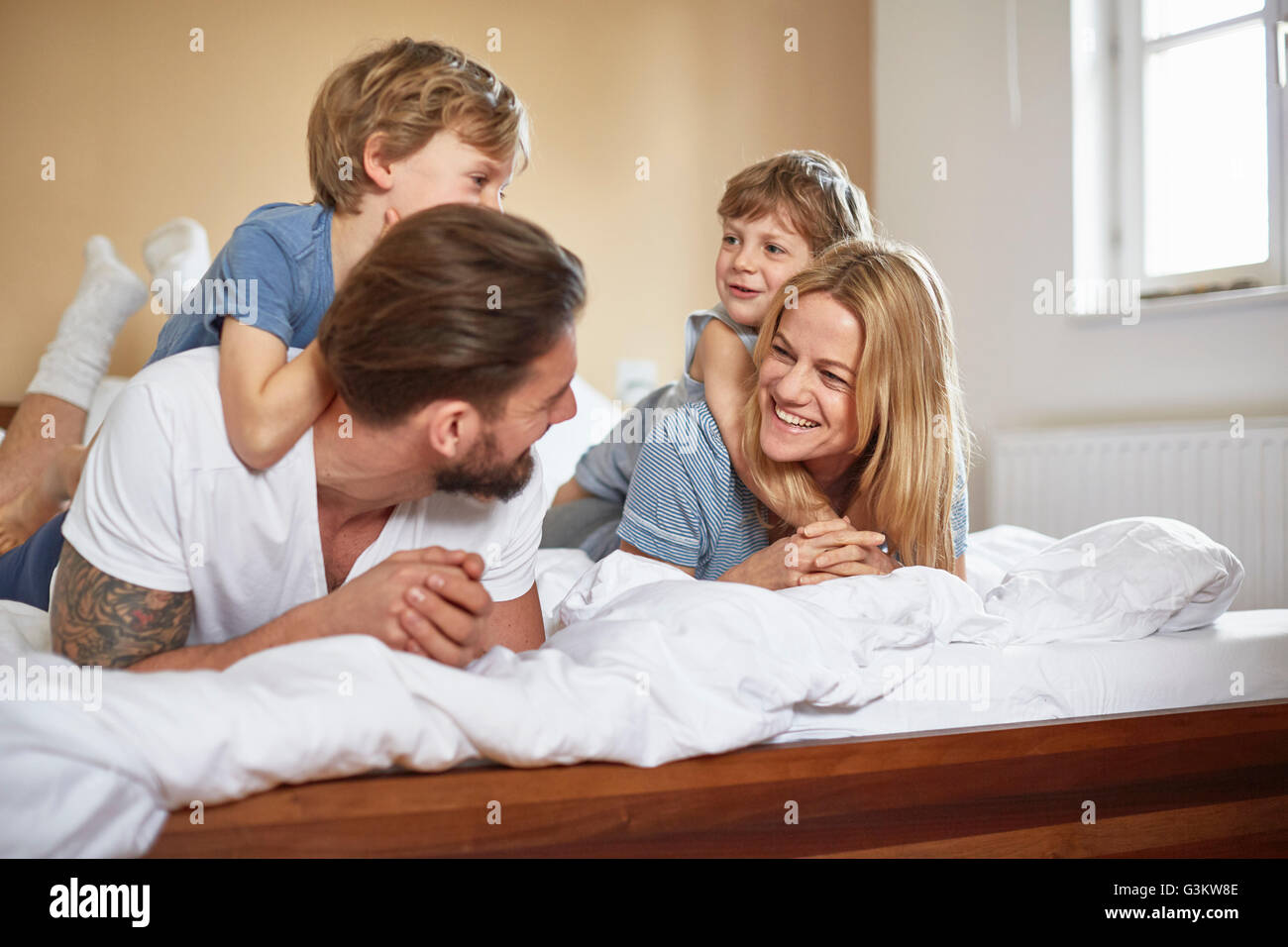 Jungs im Bett liegend auf Eltern von Angesicht zu Angesicht lächelnd Stockfoto