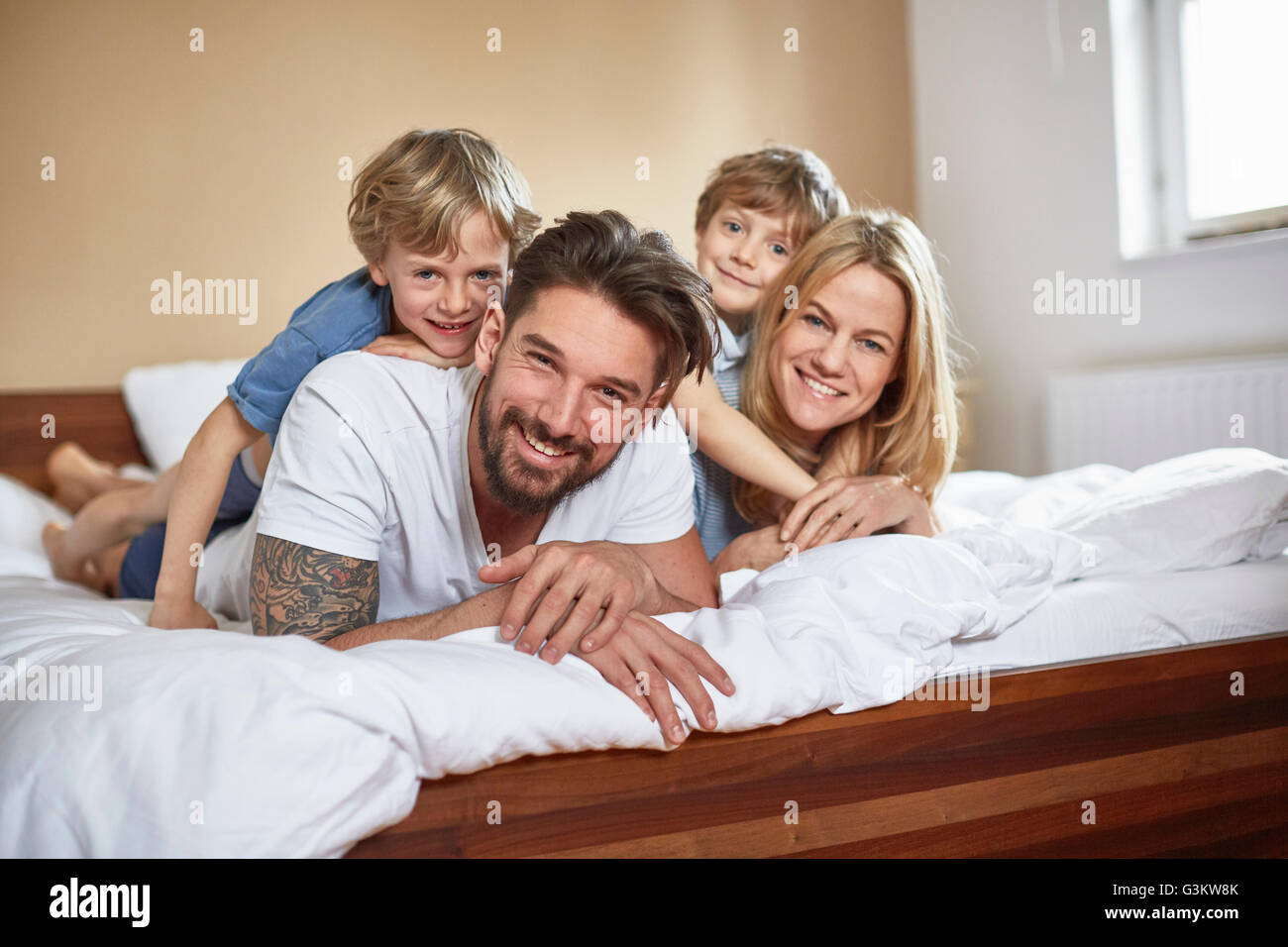 Jungs im Bett liegend auf Eltern, Blick auf die Kamera zu Lächeln Stockfoto