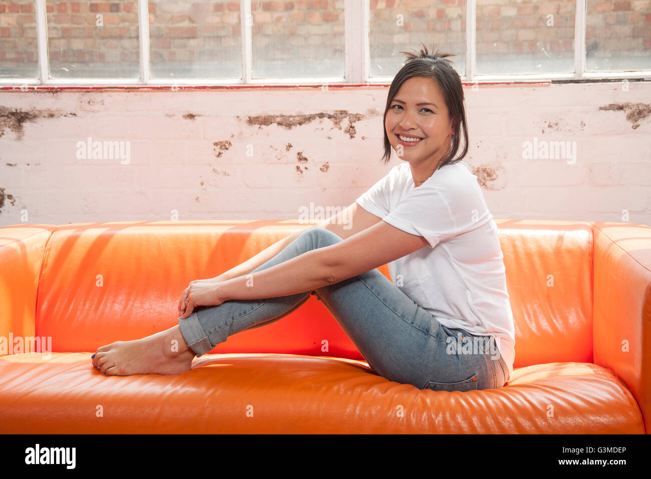 Frau sitzt auf dem Sofa mit ihren Füßen entspannt und lächelnd Stockfoto