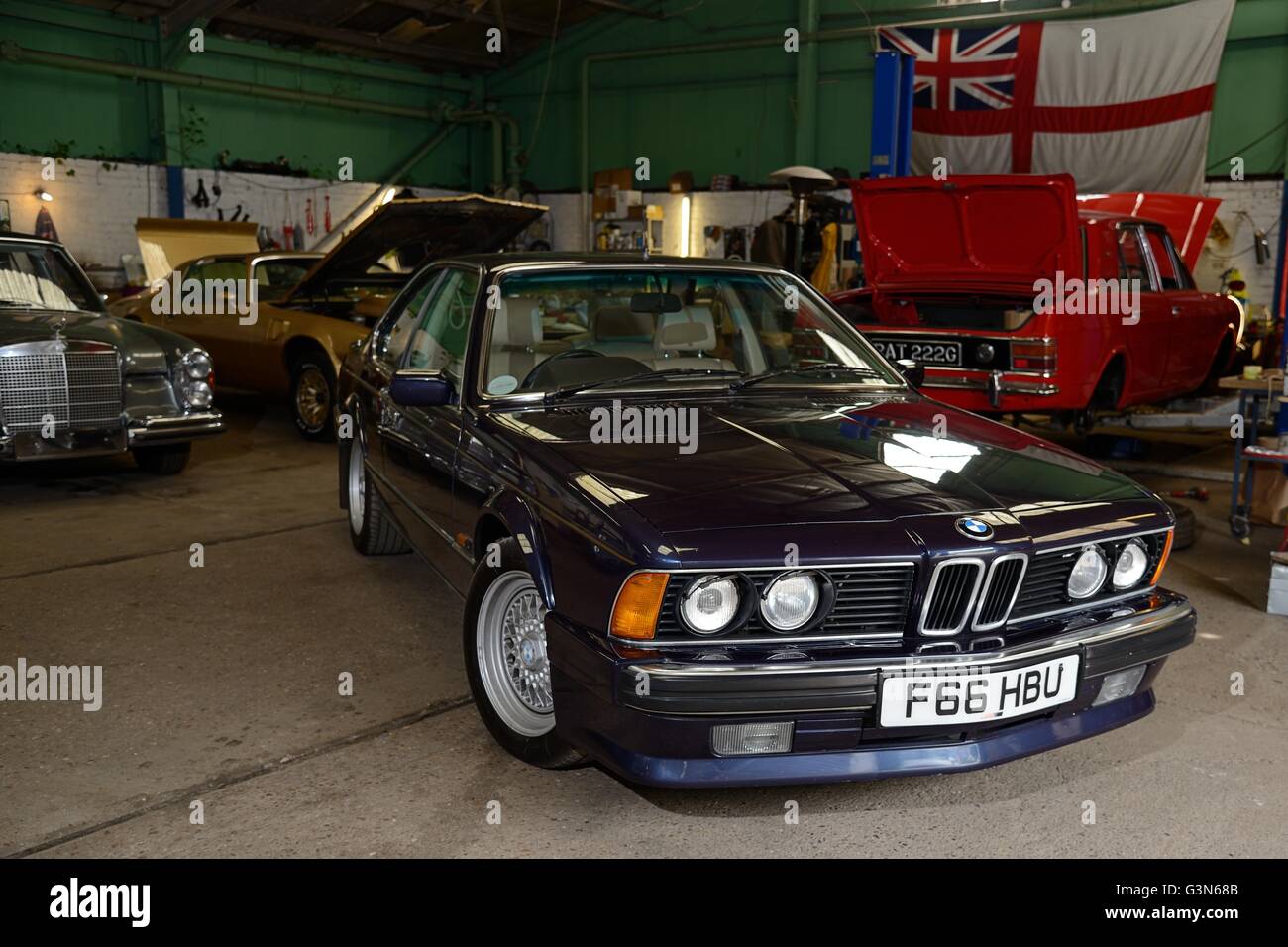 BMW 635 CSi stehen in einer Oldtimer-Werkstatt mit anderen britischen, amerikanischen und deutschen Oldtimer hinter Stockfoto