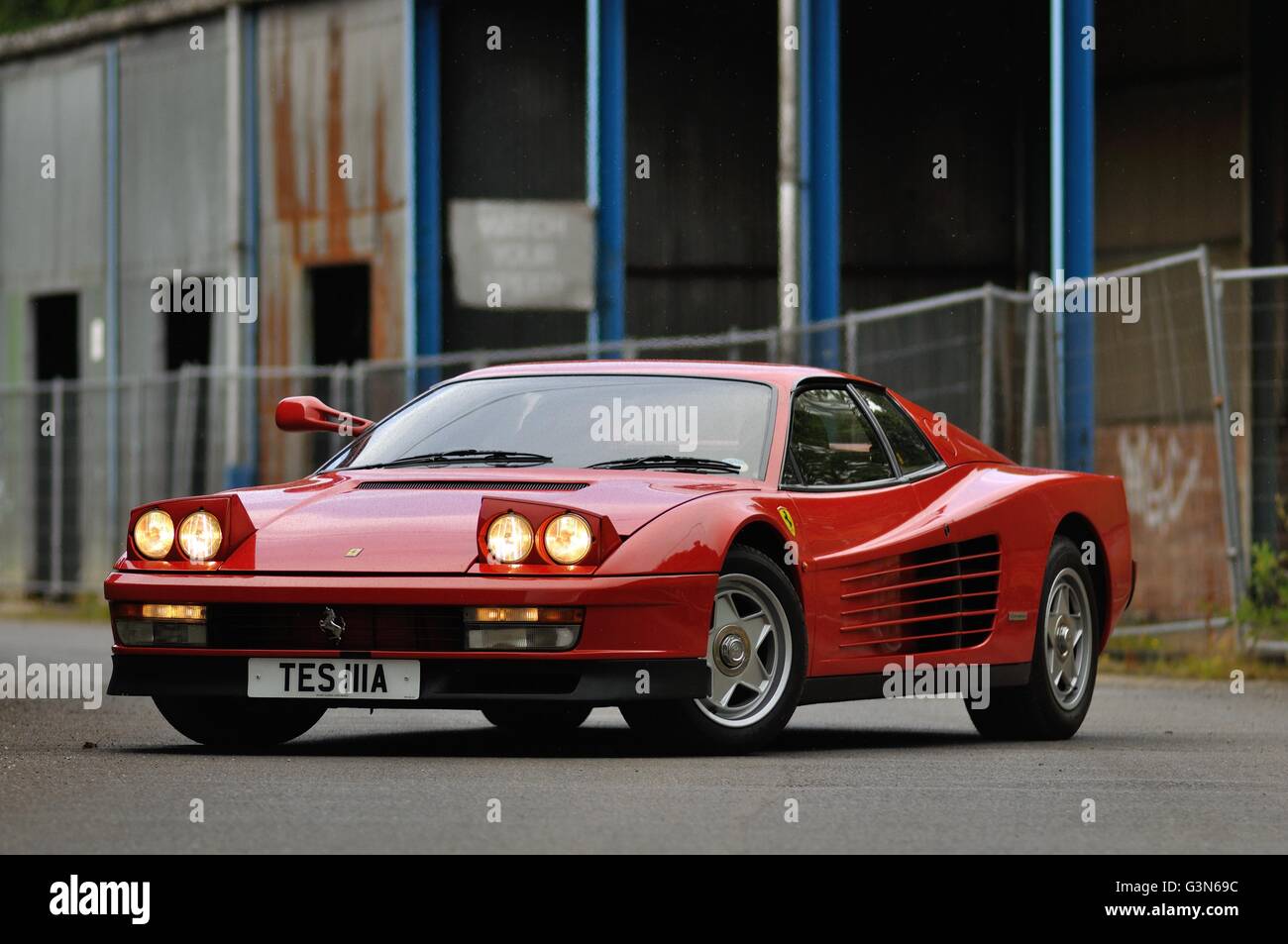 Eine 80er Jahre Ferrari Testarossa steht mit seinen Scheinwerfern auf in einem stillgelegten Industriekomplex. Stockfoto