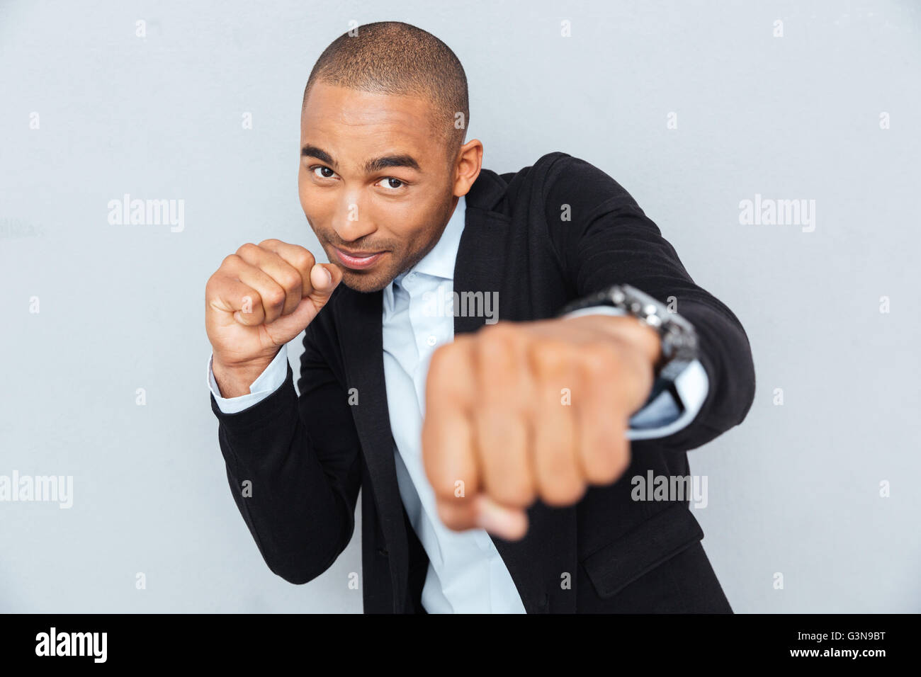 Junger Geschäftsmann stehend in Boxer-Position und bereit zu kämpfen, ballte die Fäuste und Blick in die Kamera, die isoliert auf graue backg Stockfoto