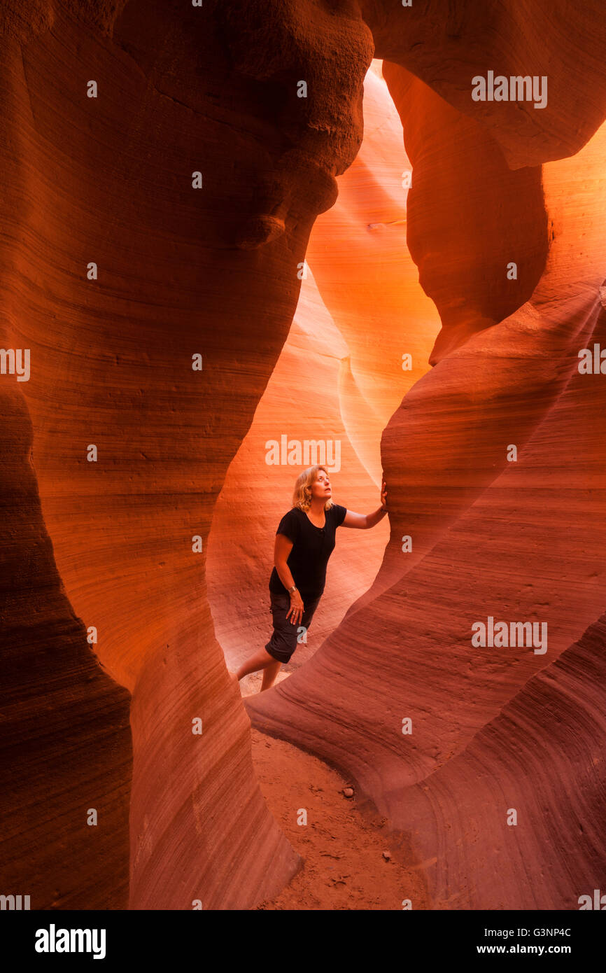 Blonde Frau schaut hinauf zum mächtigen Felsformationen wie sie die Slotcanyon im Lower Antelope Canyon, Page, AZ, USA erkundet Stockfoto