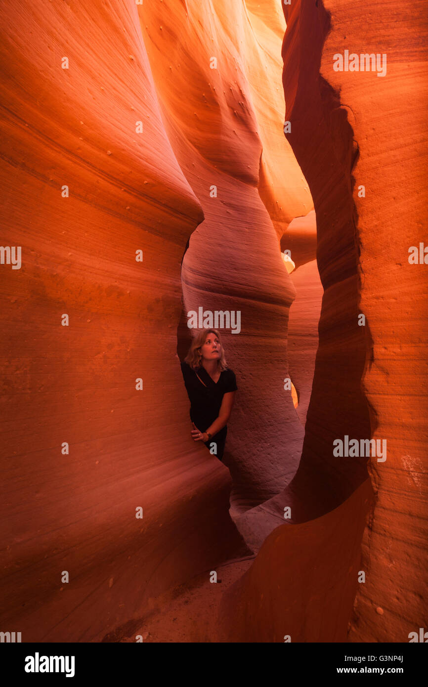 Blonde Frau schaut hinauf zum mächtigen Felsformationen wie sie die Slotcanyon im Lower Antelope Canyon, Page, AZ, USA erkundet Stockfoto