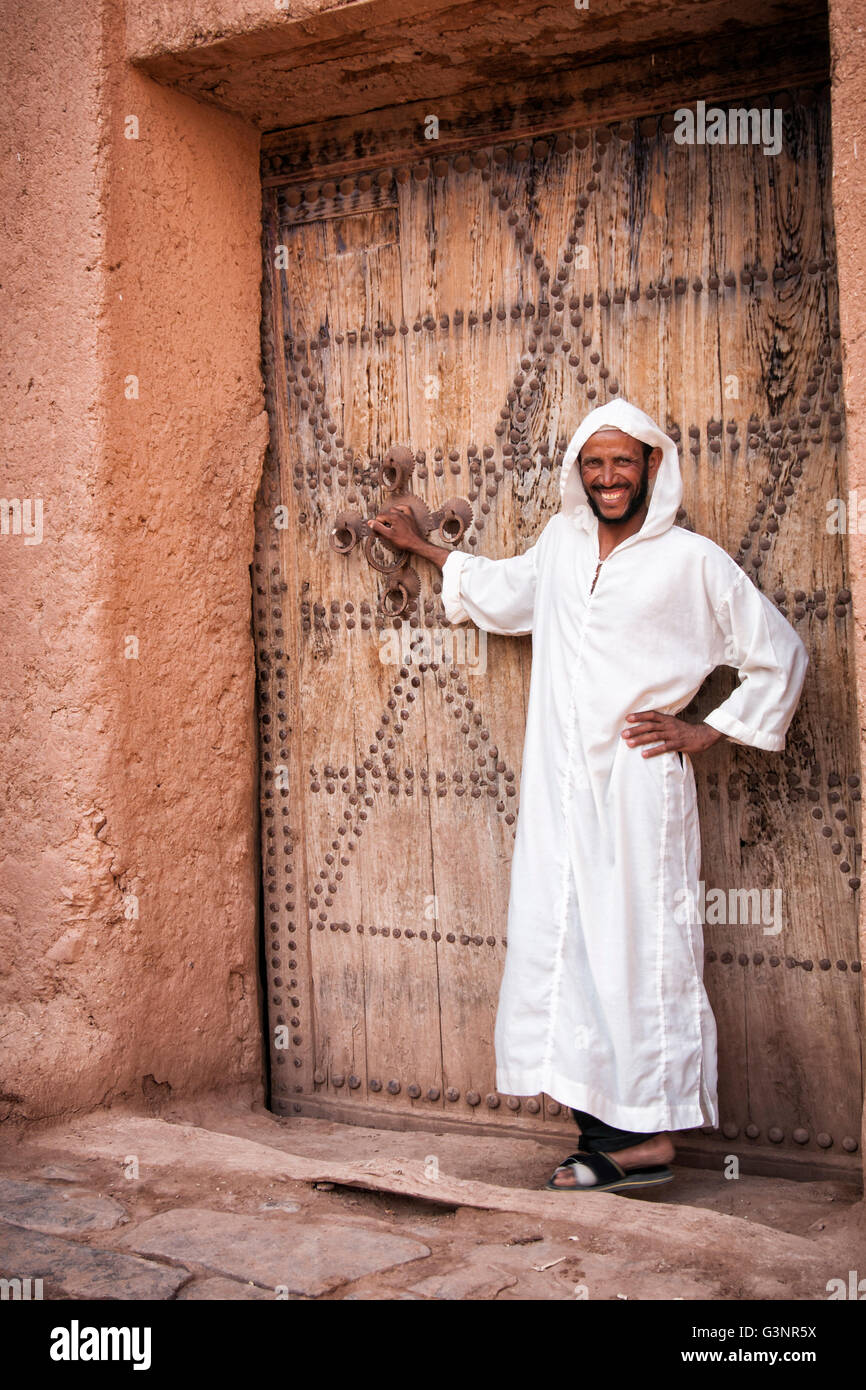 Marokkanischen Mann in langen weißen Tracht steht vor einer riesigen geschmückten alten Tür in einer Kasbah Fort, Zagora, Marokko, Stockfoto