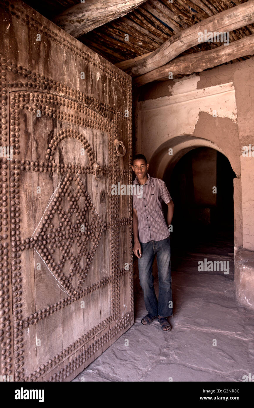 Mann in Jeans lehnt sich gegen einen riesigen geschnitzten Holztür in einer Kasbah, dass sein Großvater Handwerk als eines der 300 Gemeinschaft geholfen Stockfoto