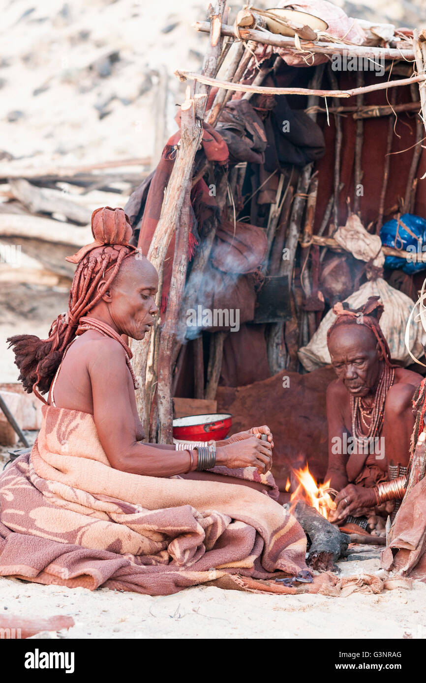 Himba Mutter und Tochter, Kazerua (90) und Venjapi (65), Rauchen außerhalb ihrer strohgedeckten, Purros Heimatdorf, Namibia, Afrika Stockfoto
