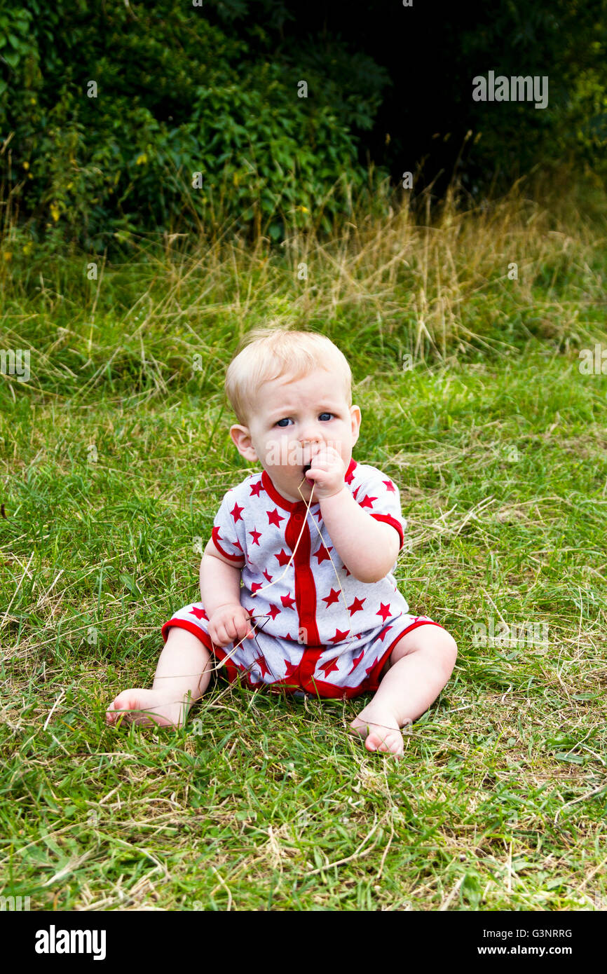 Baby auf dem Rasen sitzen und kauen auf langen Strängen Stockfoto