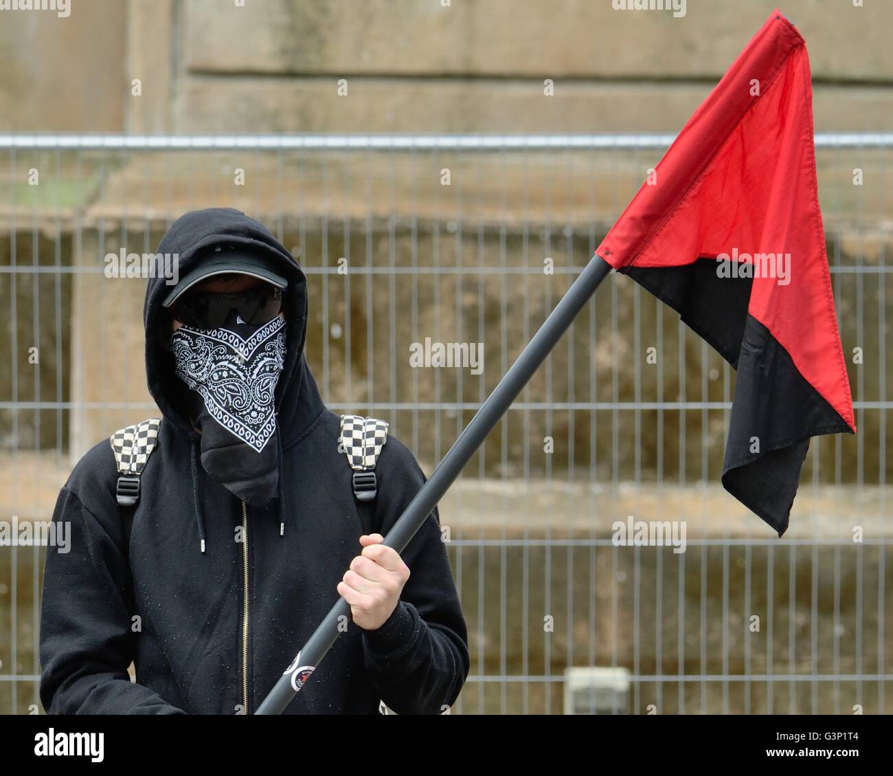 Ein Jugendlicher mit seinem Gesicht bedeckt halten eine diagonal halbierten roten und schwarzen Fahne der anarchistischen Bewegung. Stockfoto