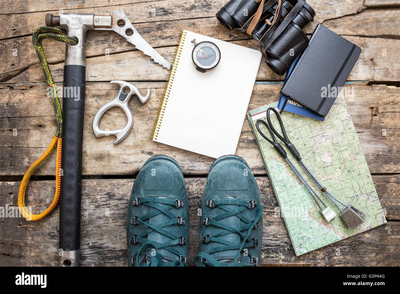 Klettern Sie Werkzeuge mit Stiefeln und Notebook auf hölzernen Hintergrund. Eis-Axt, Bergschuhe, Muttern, Kompass und Karte auf Holzbrett liegend Stockfoto
