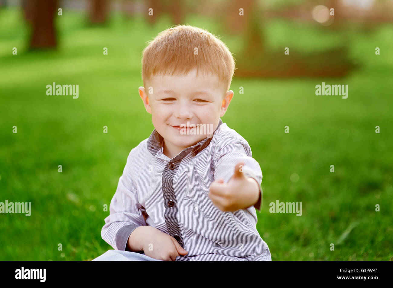 lächelnde junge sitzt auf dem grünen Rasen im Sommerpark Stockfoto