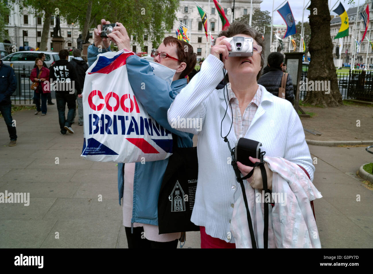 Zwei Touristen fotografieren außerhalb der Westminster Abbey. Einer hält einen Beutel mit Cool Britannia. Stockfoto