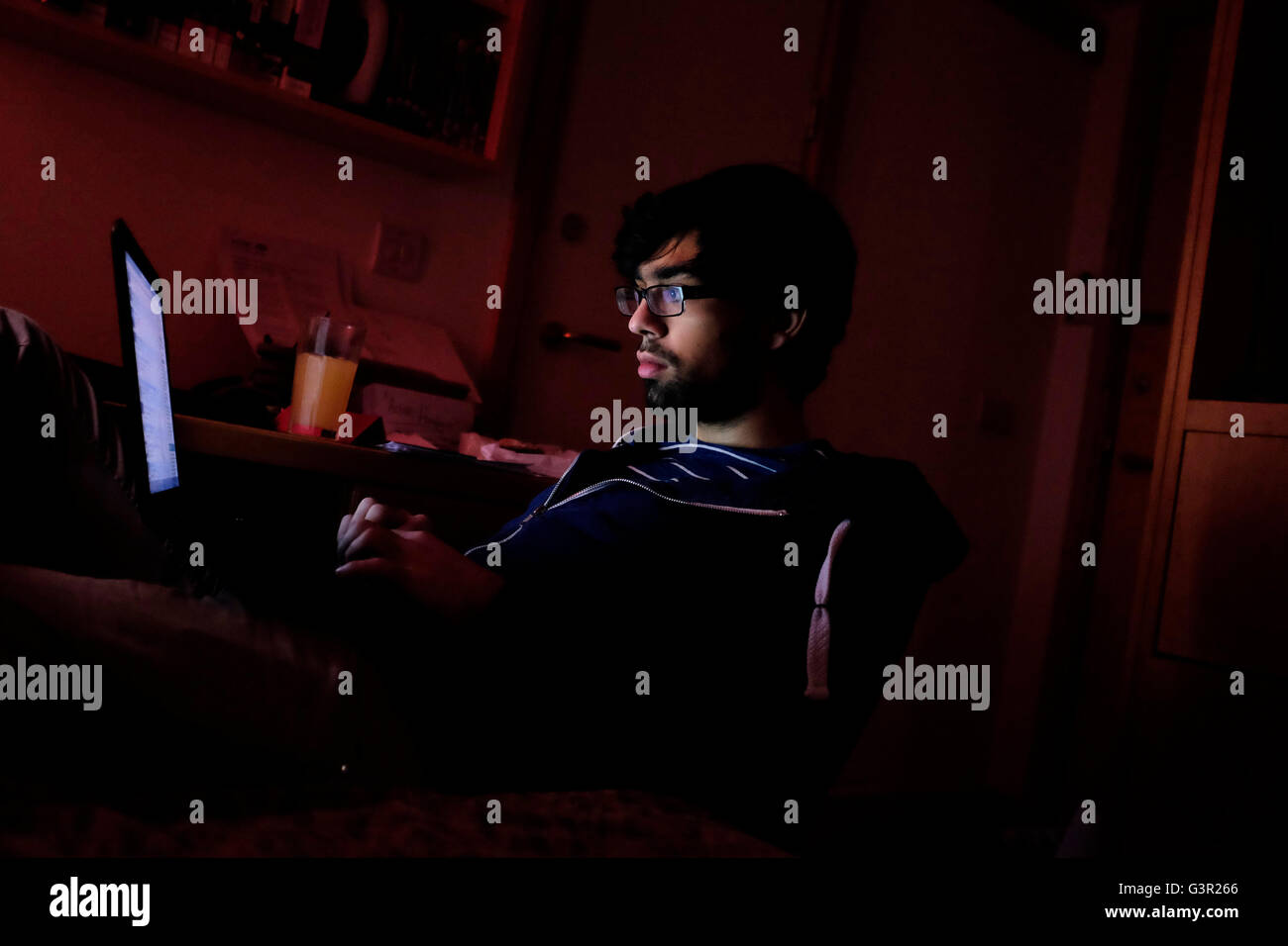 Junger Mann mit Laptop auf Knie im abgedunkelten Raum studieren Stockfoto