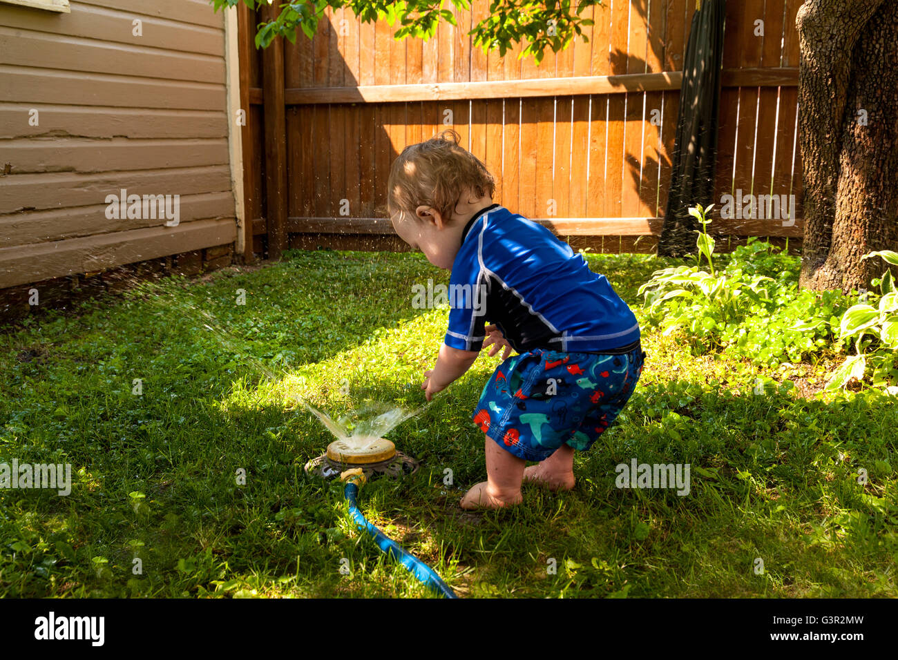 Baby-kaukasischen junge und Mutter spielen in seinem Hinterhof mit Garten sprinkler Stockfoto