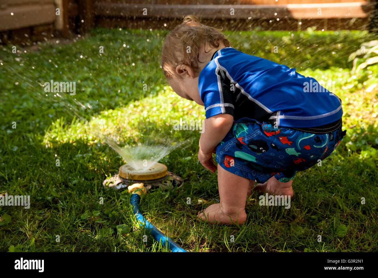 Baby-kaukasischen junge und Mutter spielen in seinem Hinterhof mit Garten sprinkler Stockfoto