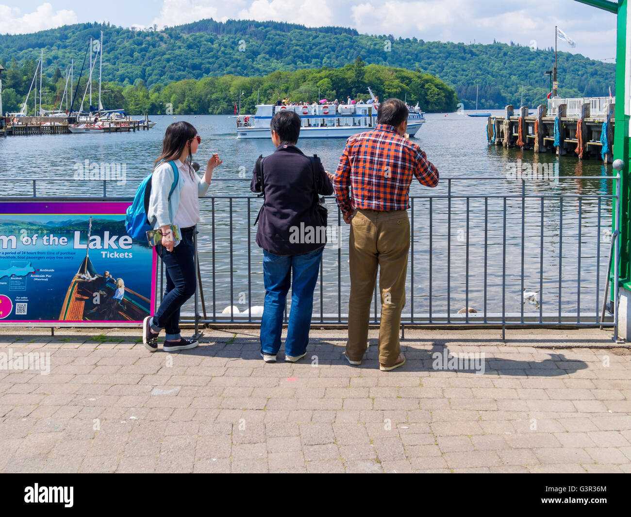 Drei asiatische Touristen beobachten die Raddampfer bei strahlendem Sonnenschein am Lake Windermere Bowness Cumbria Stockfoto