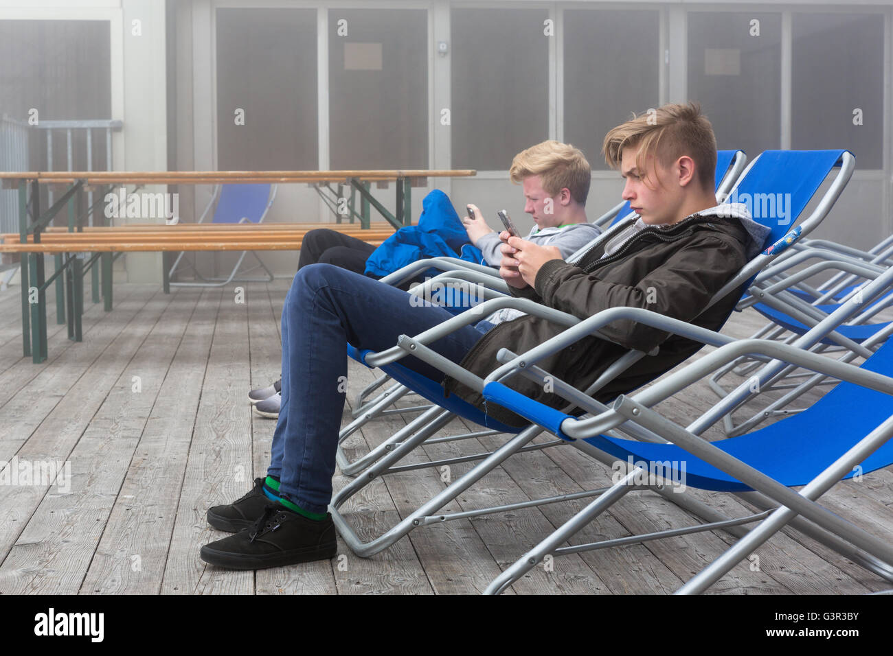 Zwei Jungs sitzen in Liegestühlen starrte auf ihren Handys Stockfoto