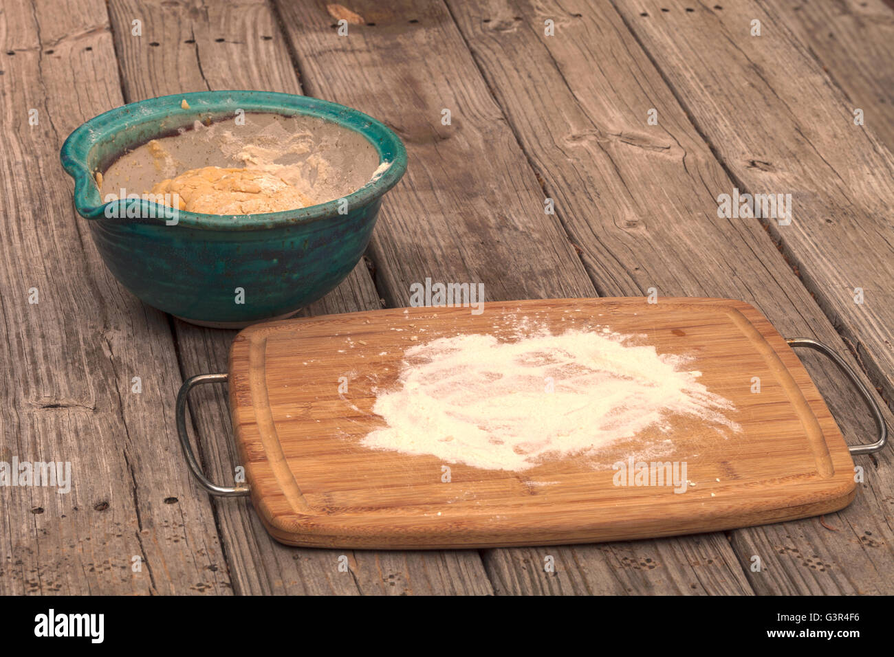 Brotbacken-Serie.  Brotteig steigt in einer Schüssel mit einem Schneidbrett mit Mehl auf einem rustikalen Picknick-Tisch zu verbreiten. Stockfoto