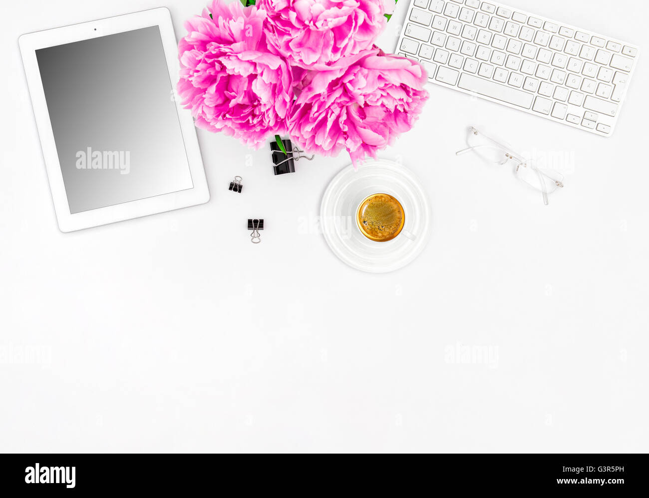 Feminine Büroarbeitsplatz mit Kaffee und Blumen. Mock-up mit digitalen Tablet-Bildschirm Stockfoto