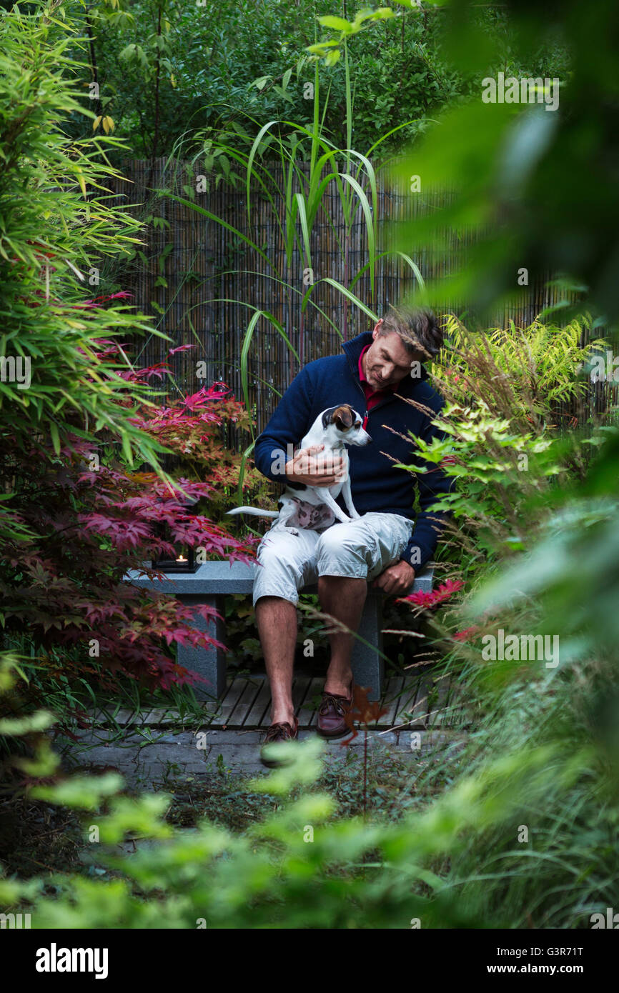 Schweden, Uppland, Mann, sitzend mit Hund auf Bank im japanischen Garten Stockfoto