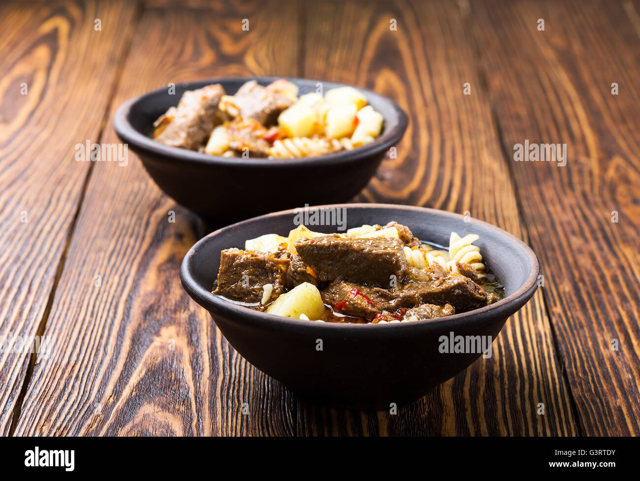 Rindergulasch mit Nudeln und Kartoffeln in Keramikschale auf Holztisch Stockfoto