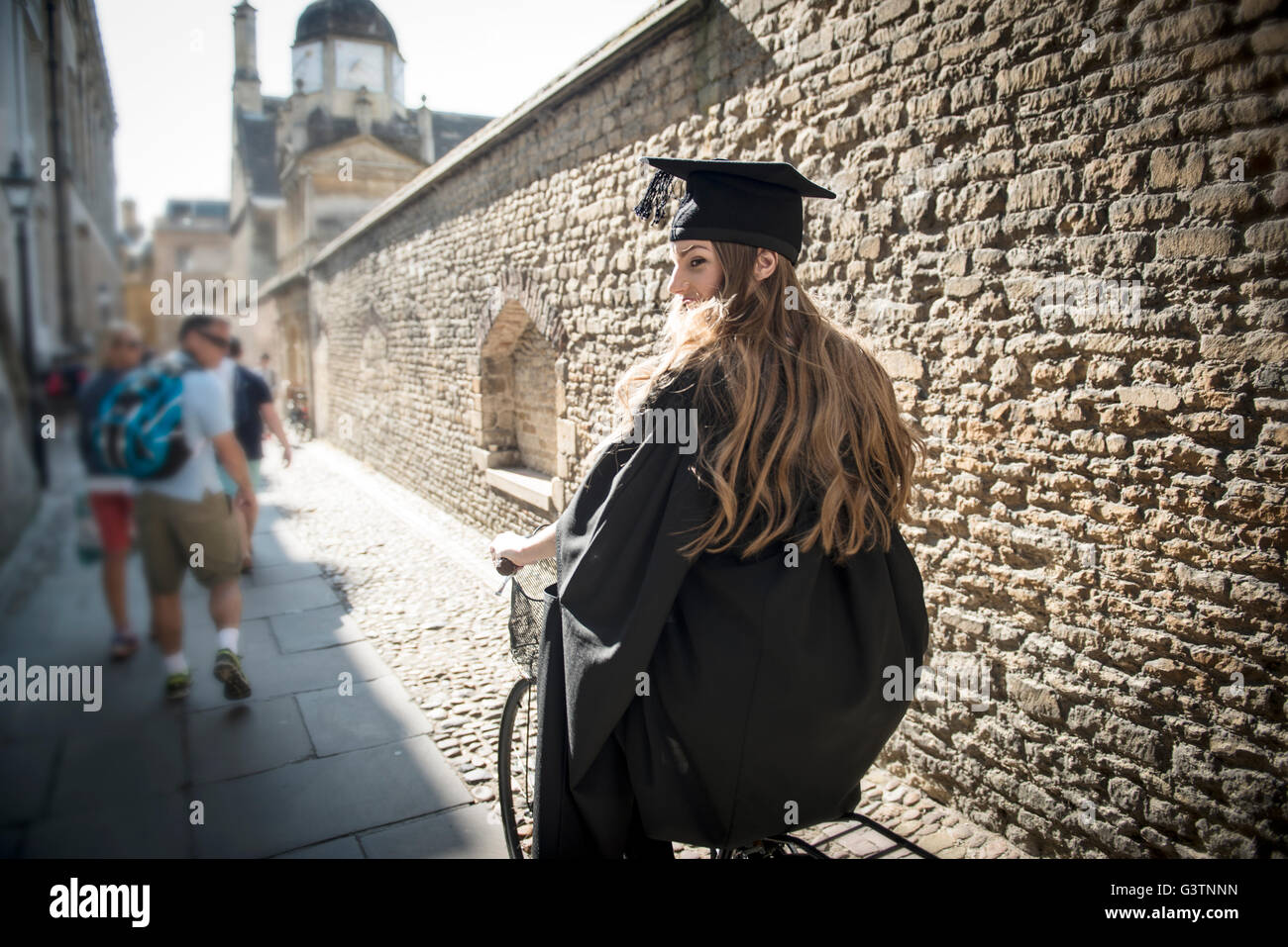 Eine Studentin in Graduierung Kleid Radfahren entlang ein Durchgang in Cambridge. Stockfoto
