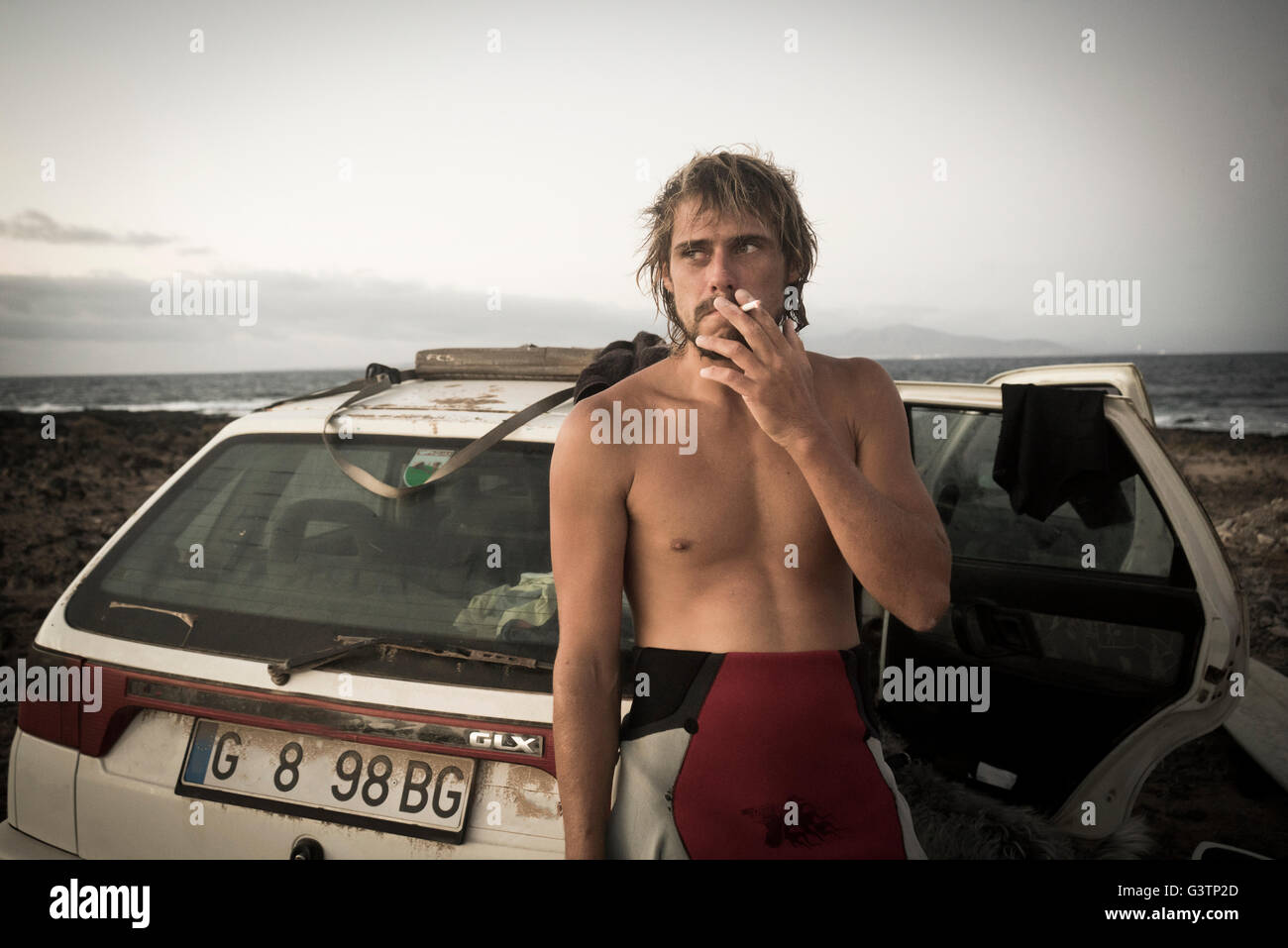 Ein Mann in einen Neoprenanzug raucht eine Zigarette durch sein Auto am Strand von Corralejo auf Fuerteventura. Stockfoto