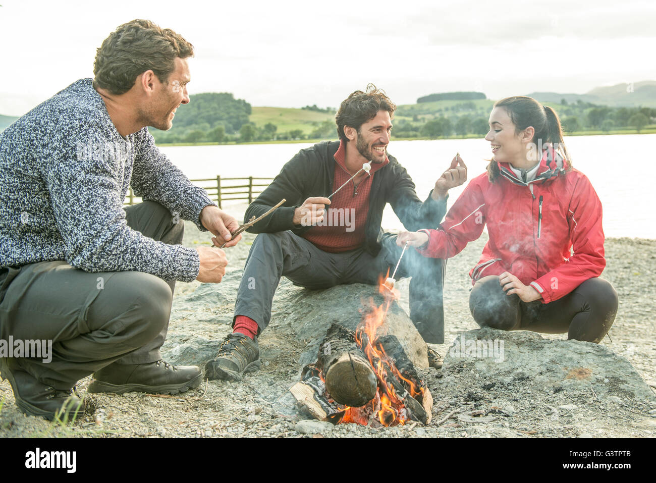 Drei Freunde entspannen um ein Lagerfeuer am Ufer des Bala See in Wales. Stockfoto