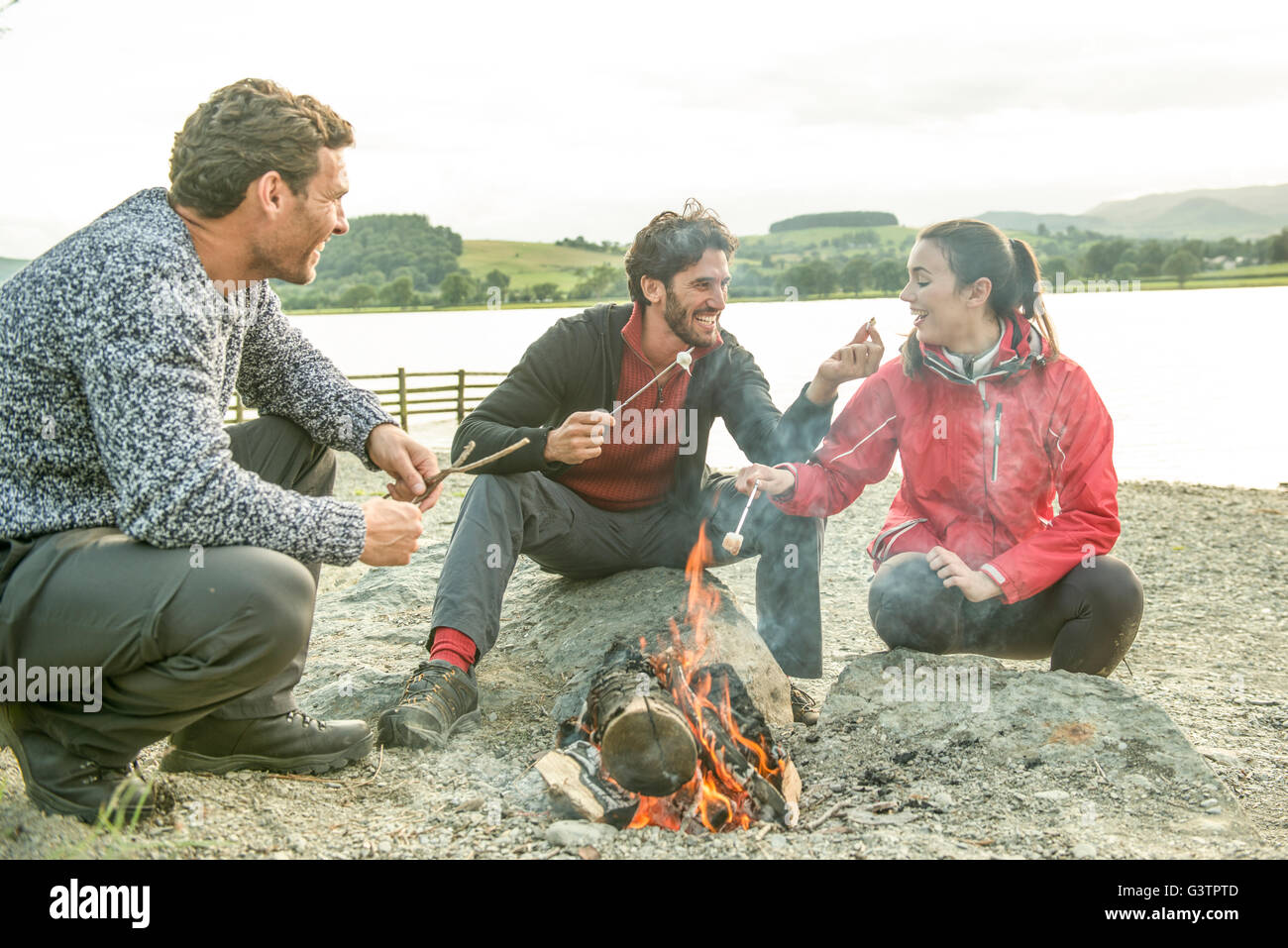 Drei Freunde entspannen um ein Lagerfeuer am Ufer des Bala See in Wales. Stockfoto