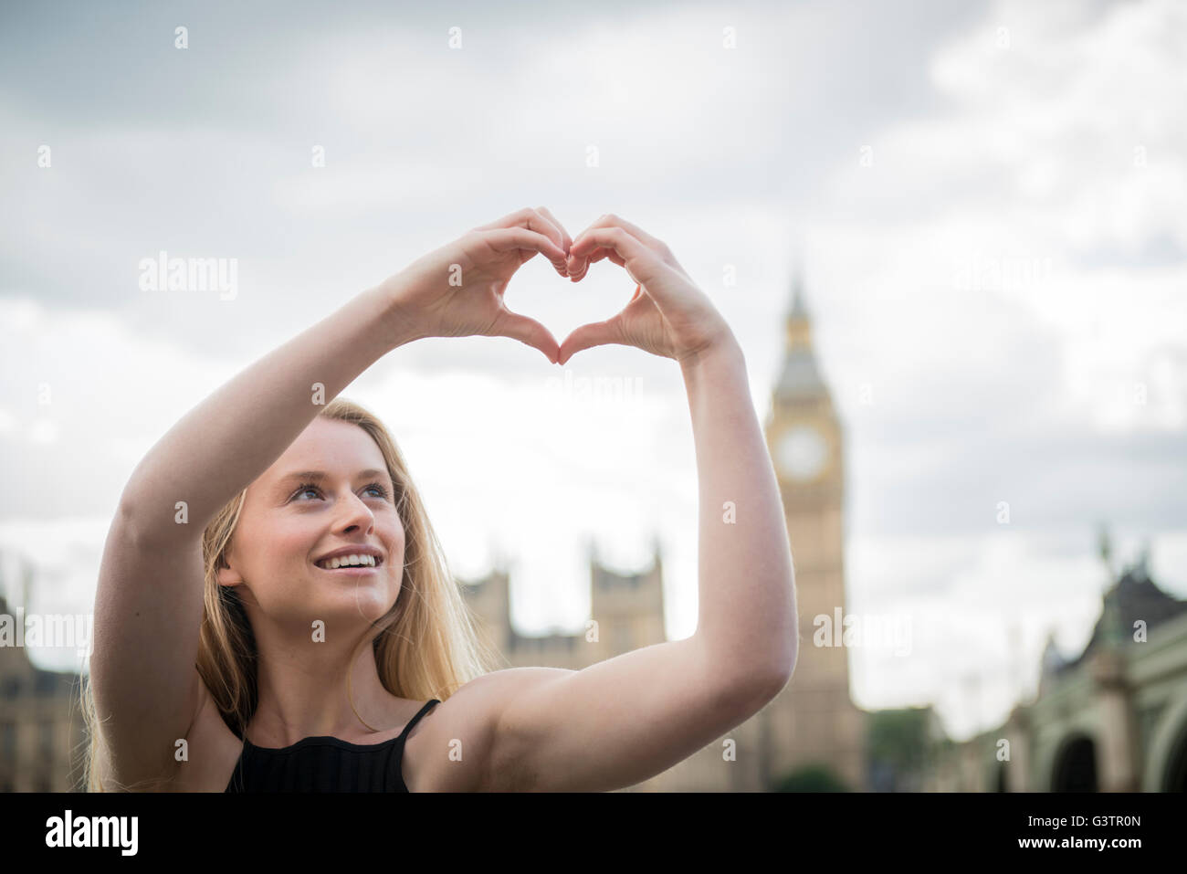 Eine junge Frau macht eine Herzform mit den Händen mit den Houses of Parliament im Hintergrund. Stockfoto