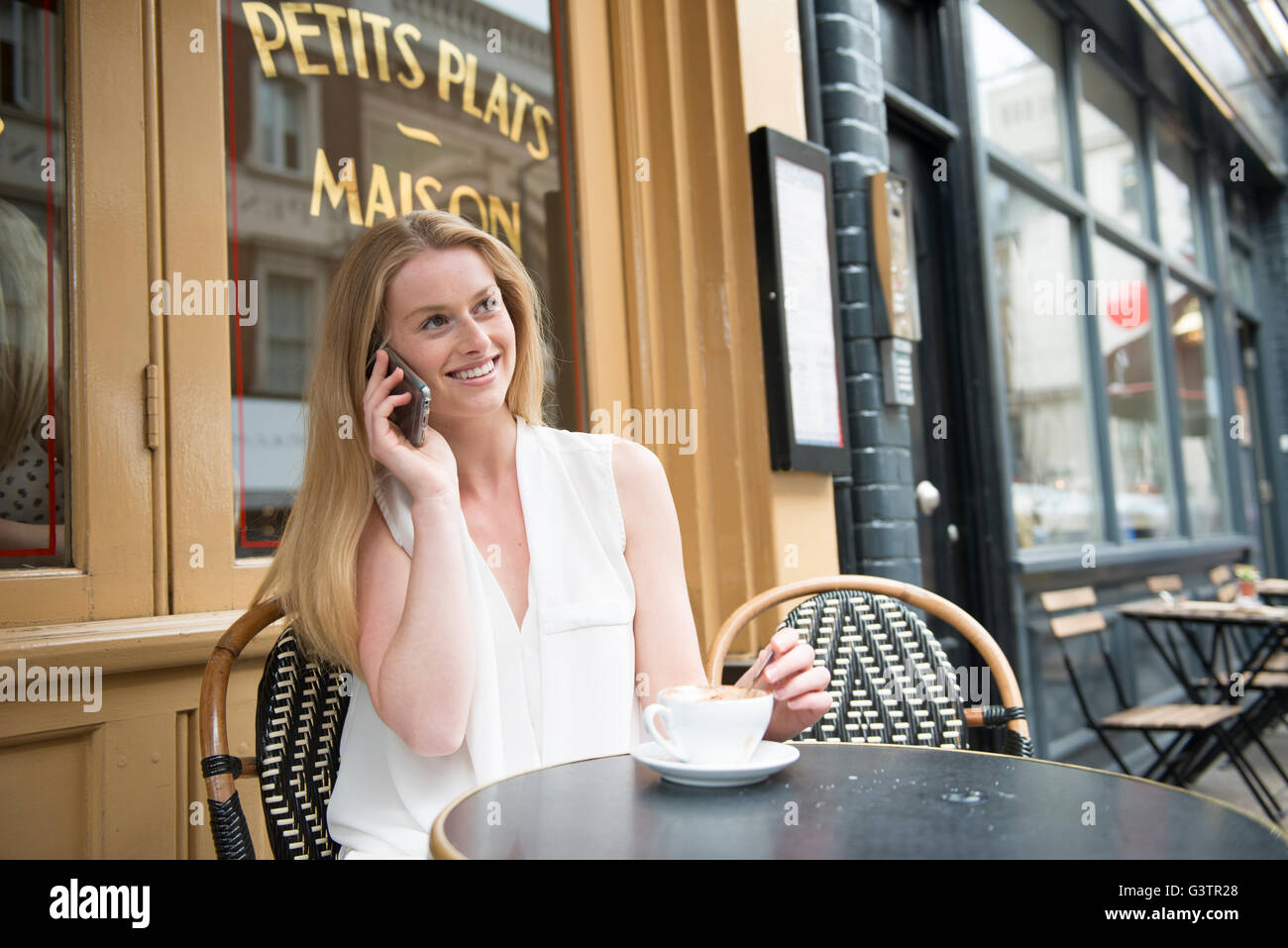 Eine junge Frau sitzt vor einem Café auf dem Handy in Covent Garden in London. Stockfoto