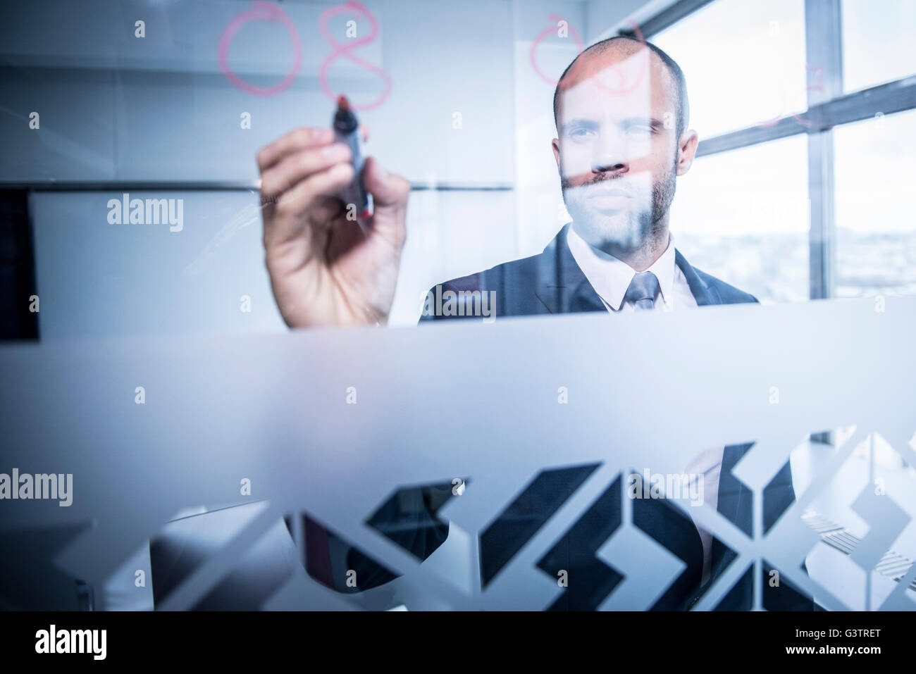 Ein professioneller Mann schreiben von Zahlen auf Glas in einer Büroumgebung. Stockfoto