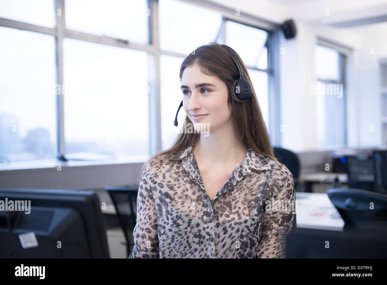 Eine junge berufstätige Frau in einer Büroumgebung Anrufe über einen Kopfhörer empfangen. Stockfoto