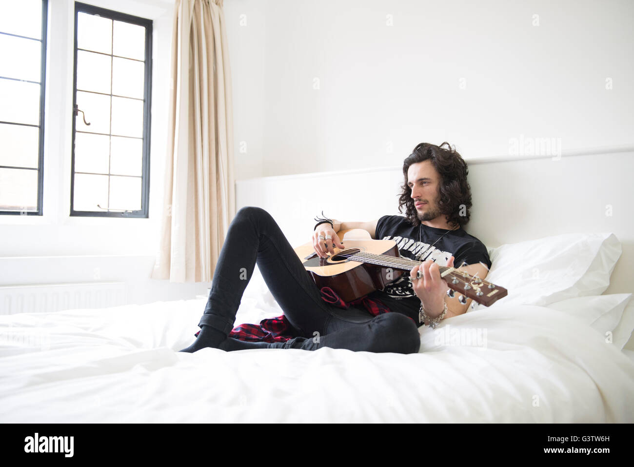 Ein cooler junger Mann mit auf einem Bett mit einer Gitarre. Stockfoto
