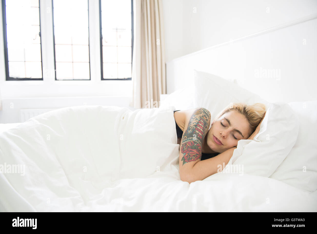 Eine coole junge tätowierte Frau schläft in einem Bett. Stockfoto