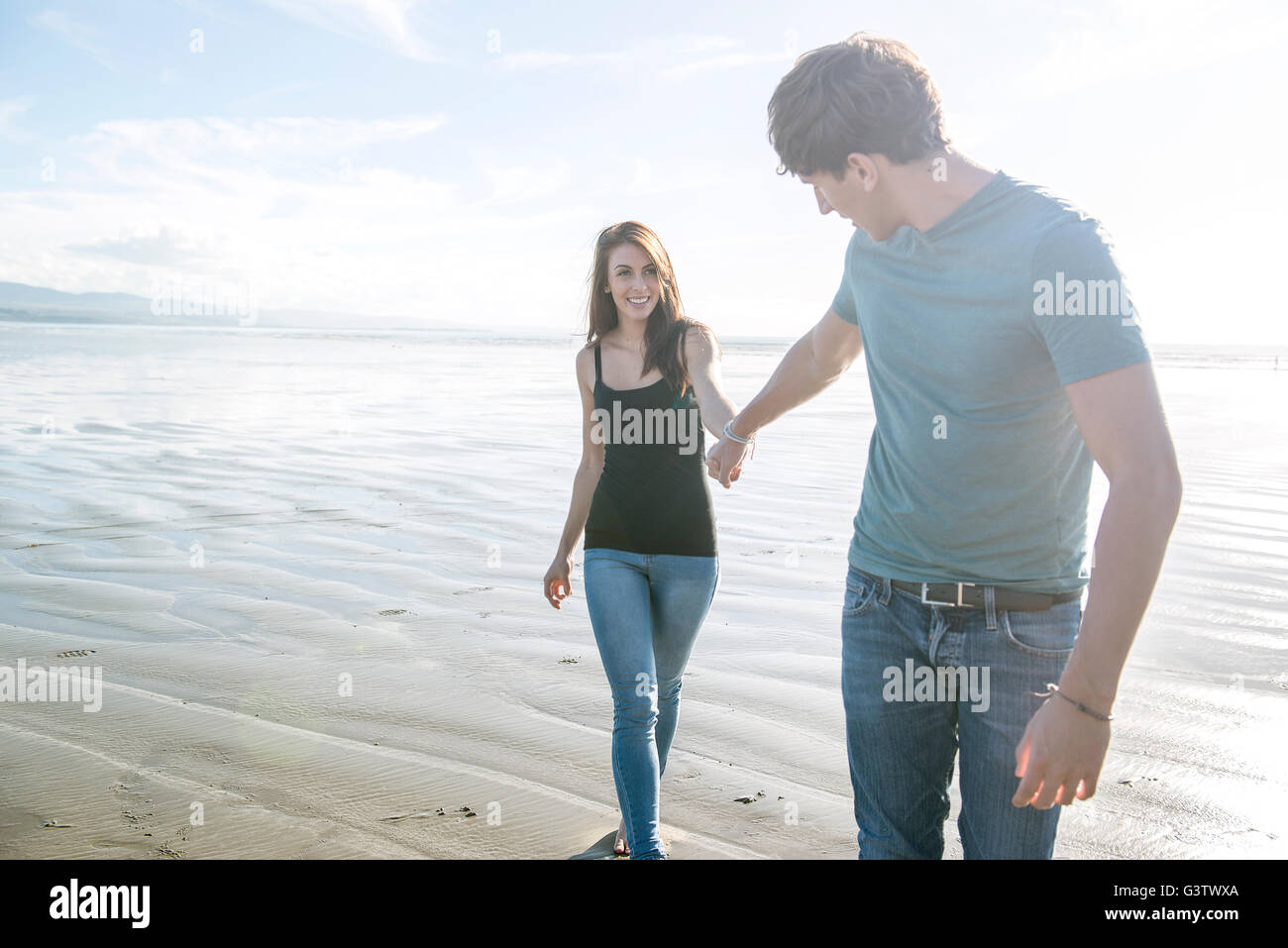 Ein junges Paar gehen Hand in Hand über den Strand von Porthmadog. Stockfoto