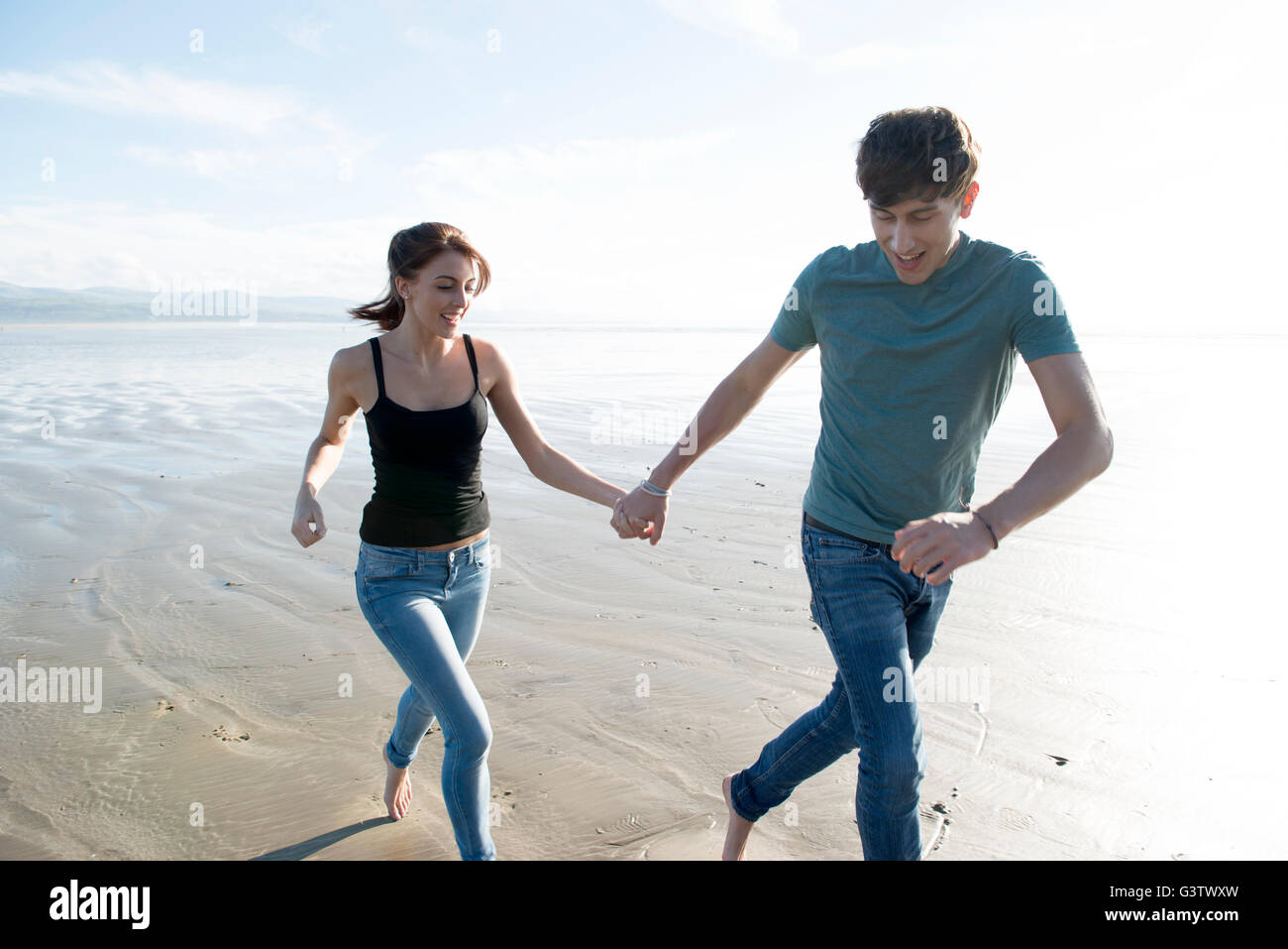 Ein junges Paar laufen, während die Hände am Strand von Porthmadog halten. Stockfoto